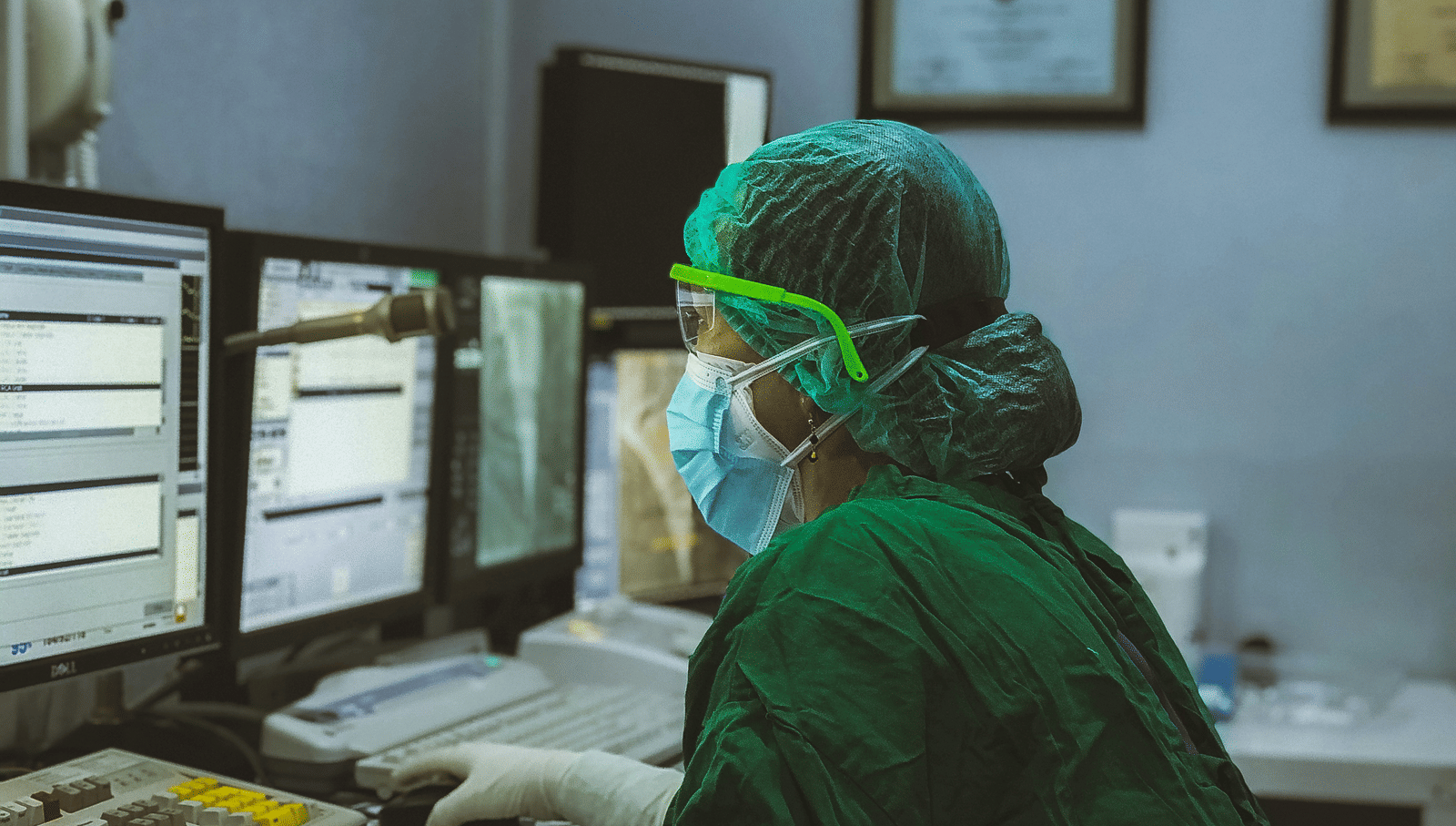 A healthcare worker wearing PPE and looking into the computer in a medical office.